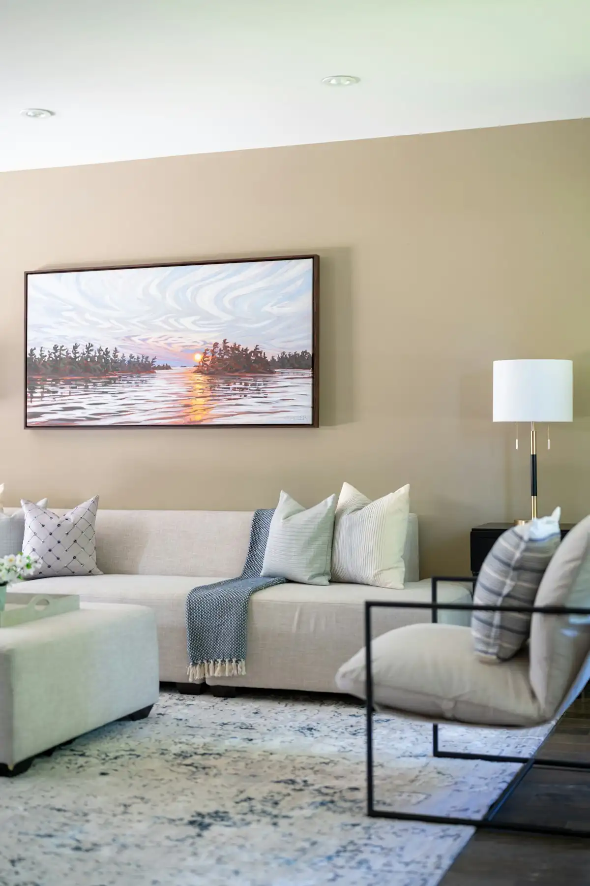 Tableaux de paysage et décoration intérieure : comment la perspective crée de la profondeur dans une pièce Grand tableau panoramique d'un coucher de soleil sur un lac accroché au mur beige d'un salon moderne au-dessus d'un canapé clair